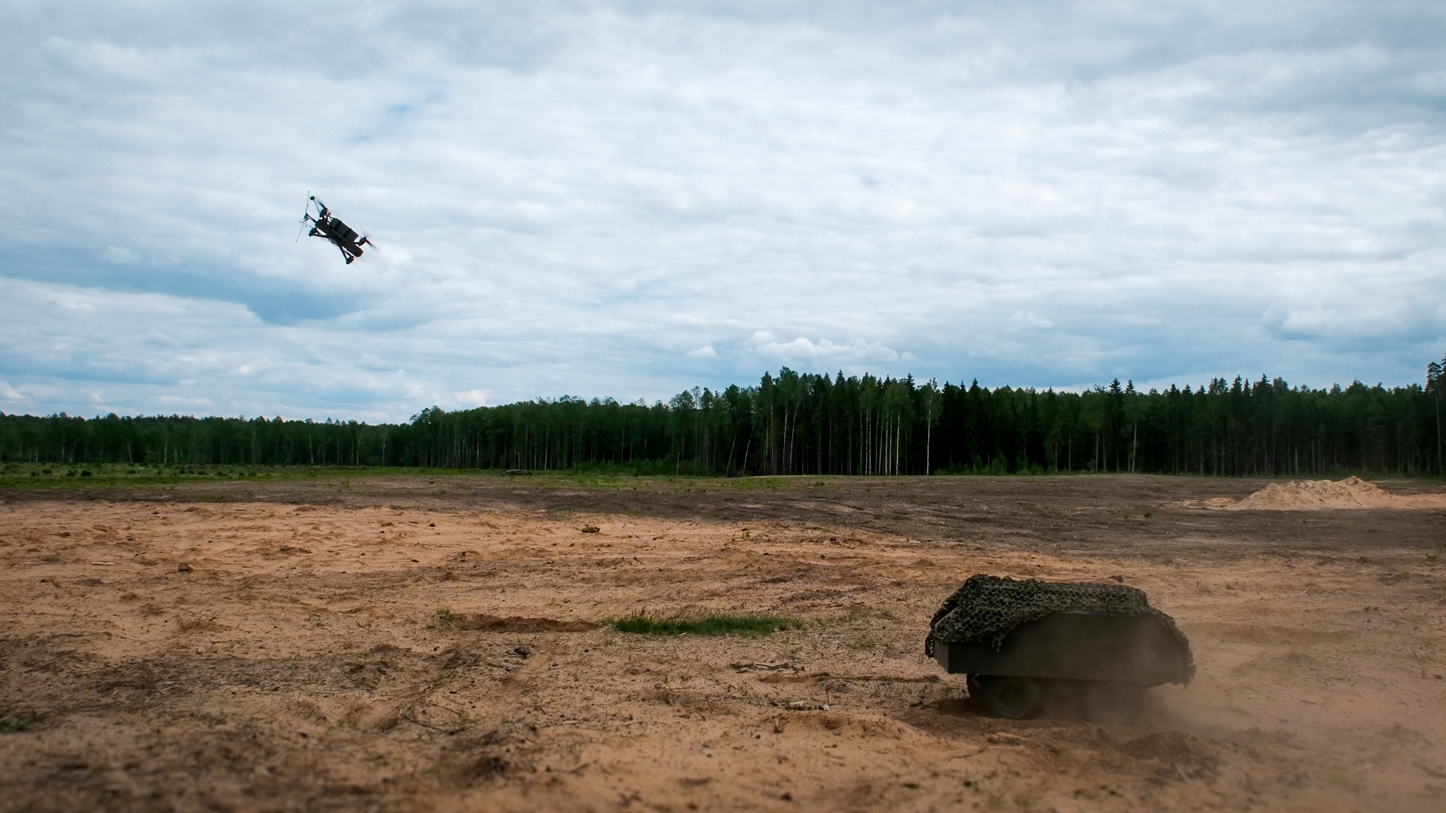 Aerial drone engaging with an unmanned ground vehicle in a military training range.