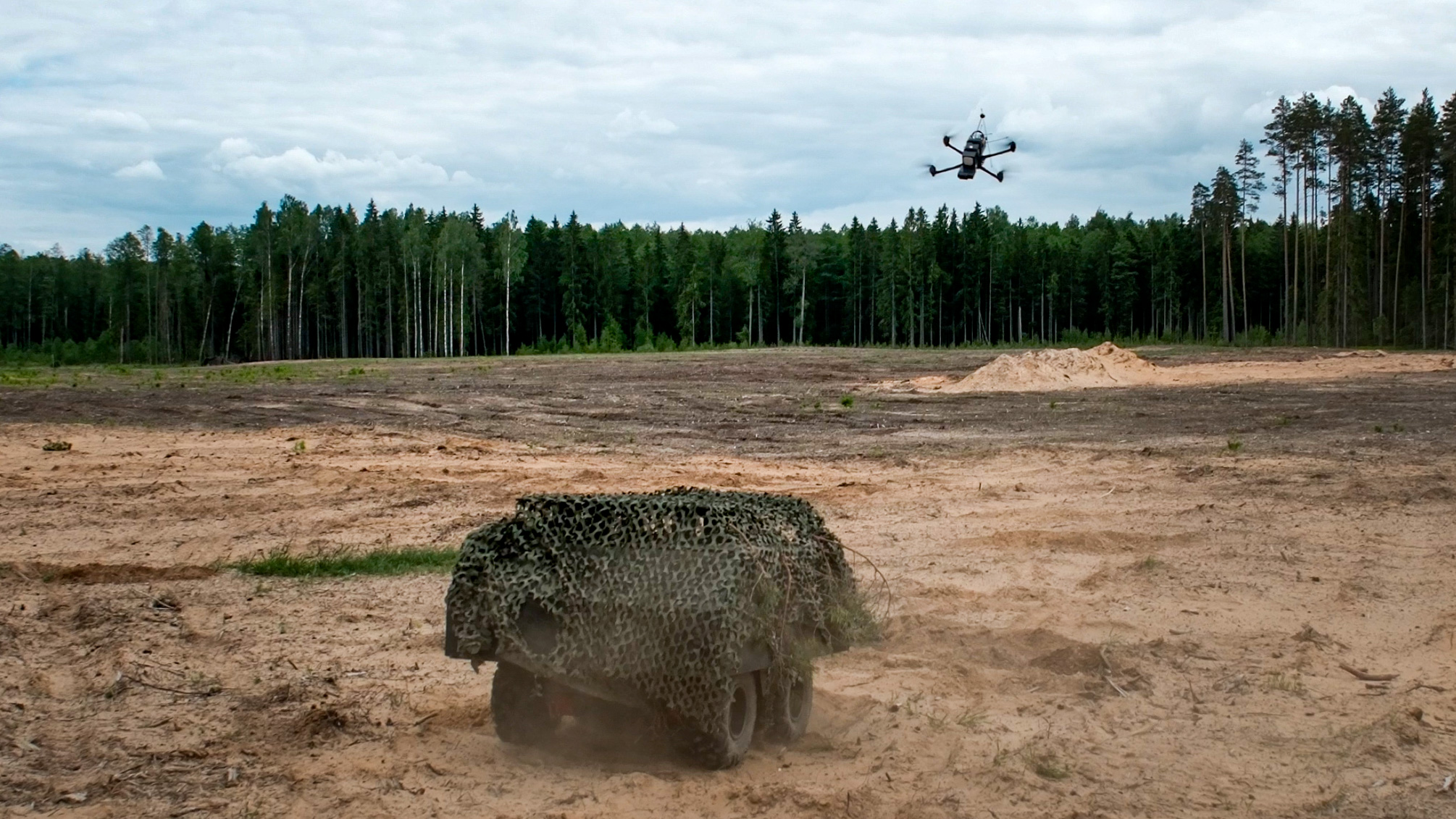 Military training ground. A flying drone is monitoring an unmanned ground vehicle.